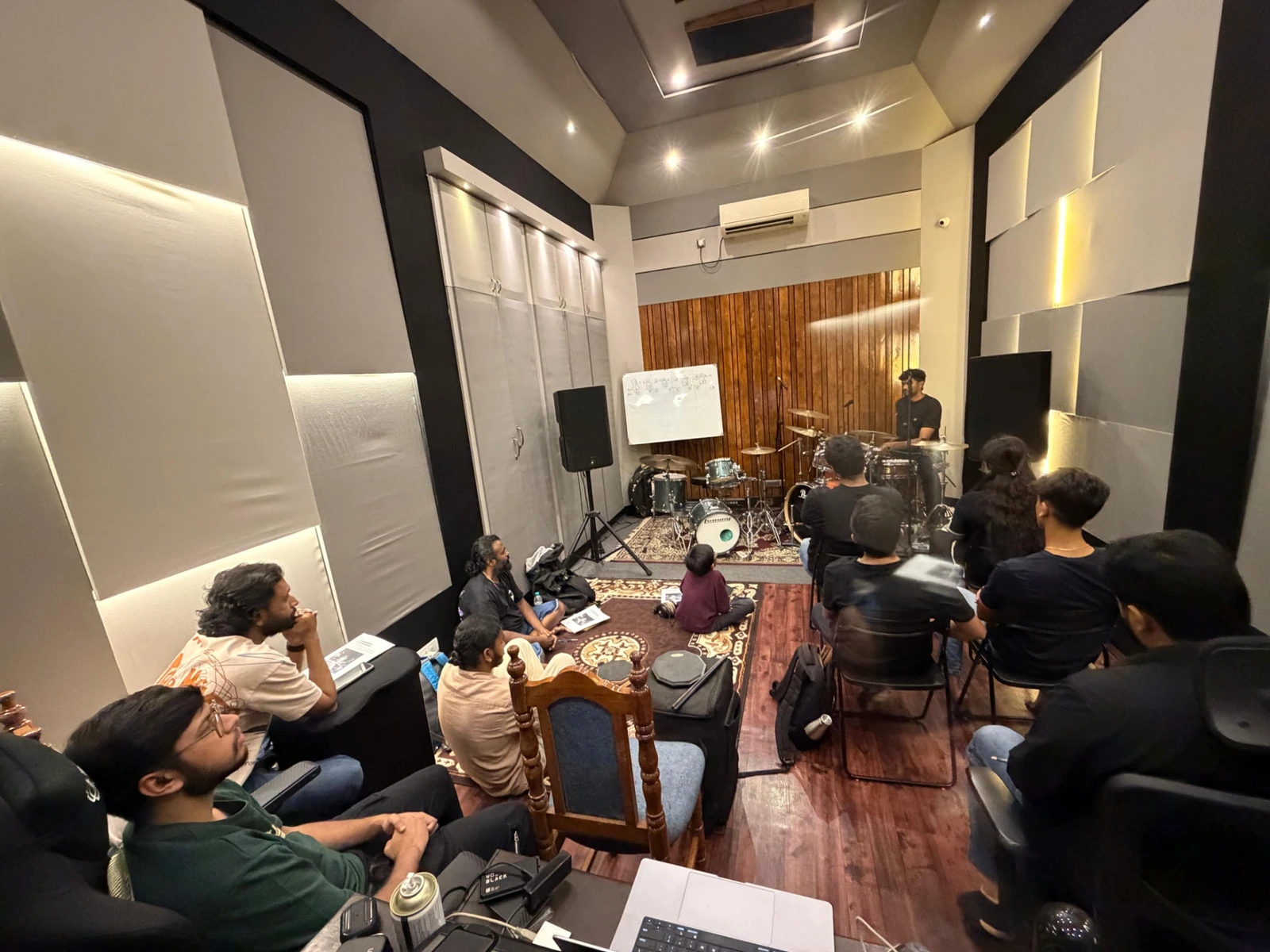 Drum workshop in session with students seated around the kit in the treated studio room